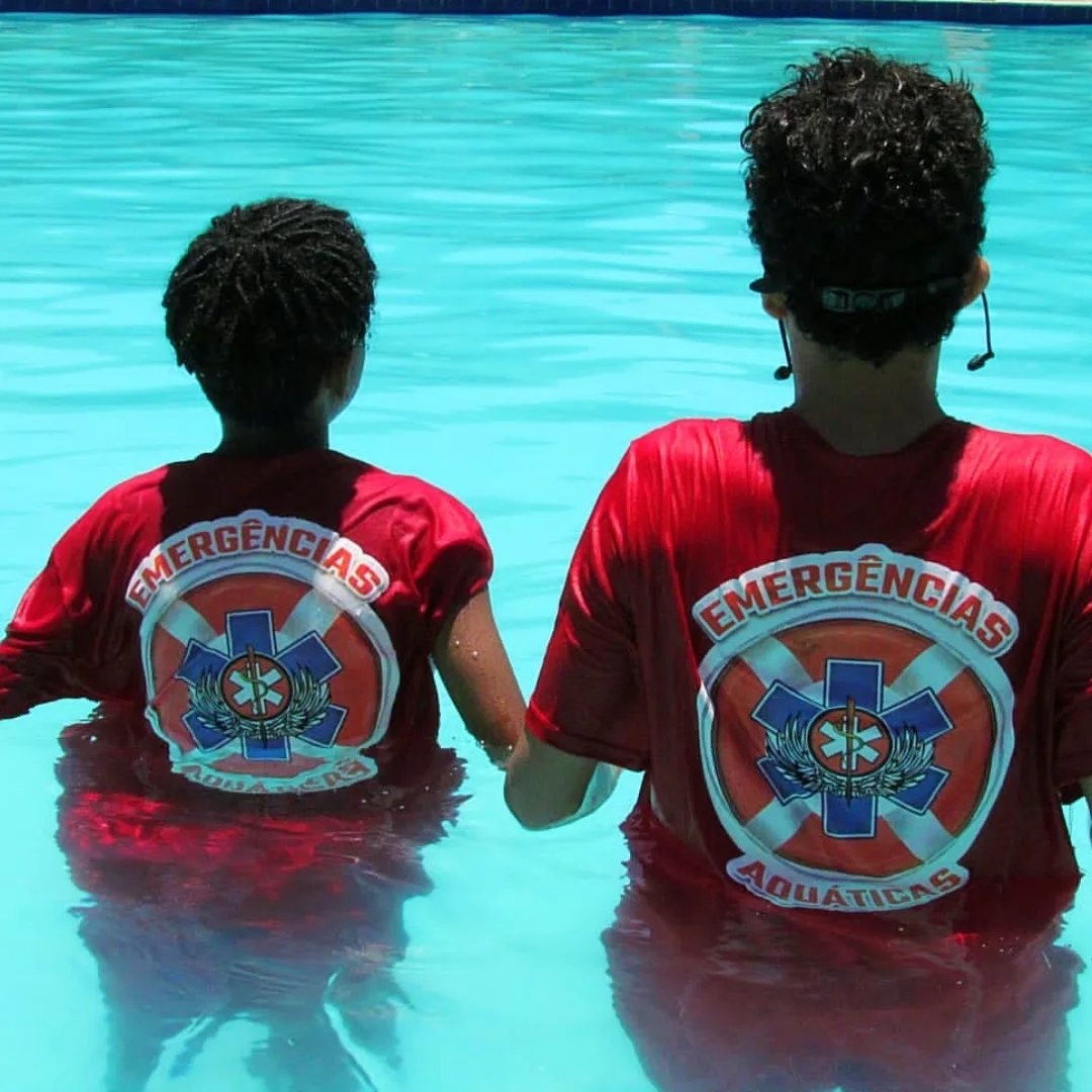 Dois alunos com camisa de Emergências Aquáticas dentro da piscina
